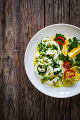 Fried calamari rings with lemon, greens and cherry tomatoes on wooden table
