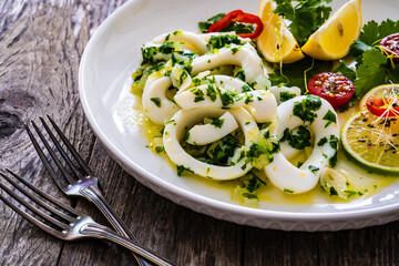 Fried calamari rings with lemon, greens and cherry tomatoes on wooden table
