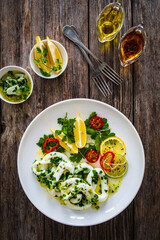 Fried calamari rings with lemon, greens and cherry tomatoes on wooden table
