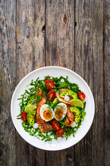 Salmon salad - smoked salmon, hard boiled eggs, avocado and leafy greens on wooden table
