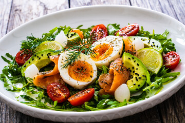 Salmon salad - smoked salmon, hard boiled eggs, avocado and leafy greens on wooden table
