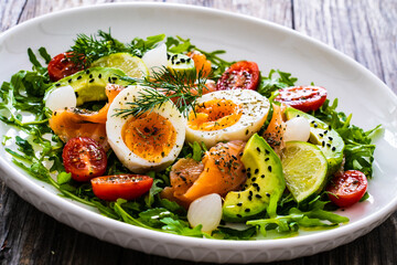 Salmon salad - smoked salmon, hard boiled eggs, avocado and leafy greens on wooden table
