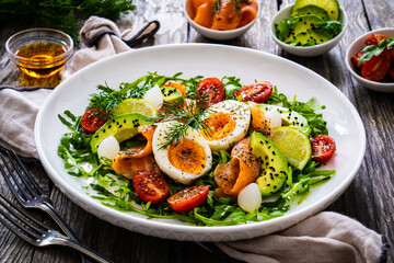 Salmon salad - smoked salmon, hard boiled eggs, avocado and leafy greens on wooden table
