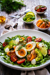 Salmon salad - smoked salmon, hard boiled eggs, avocado and leafy greens on wooden table
