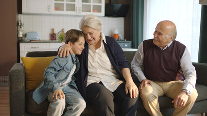 Little boy visiting his grandparents. Happy elderly couple sitting on sofa and chatting with their...