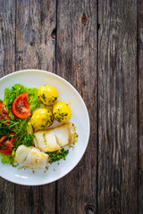 Fish dish - fried halibut with boiled potatoes and fresh vegetables on wooden table
 - obrazy, fototapety, plakaty