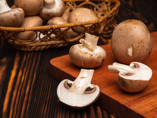 champignon mushrooms on a cutting board and on a dark wood table