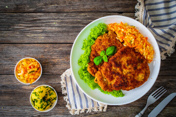 Breaded fried pork chop with cabbage salad and greens on wooden table

