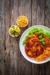 Breaded fried pork chop with cabbage salad and greens on wooden table
