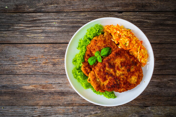 Breaded fried pork chop with cabbage salad and greens on wooden table
