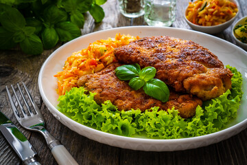 Breaded fried pork chop with cabbage salad and greens on wooden table

