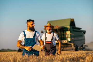 Grandfather and grandson, satisfied with the harvest, walk towards each other in the wheat field,...
