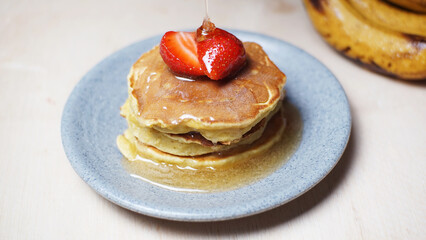 Stack of traditional banana pancakes with delicious strawberry slices and honey