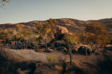 Panorama kurz nach Sonnenaufgang - Blick auf einen Camping Stellplatz im Erongo-Gebirge, auf der gerade eine Familie mit altem Geländewagen campt, Namibia