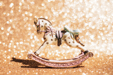 Vintage rocking horse figurine standing on a sparkling gold background. A Christmas composition for...