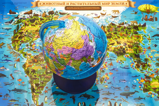 The school globe stands on the geographical atlas of the earth with images of animals
