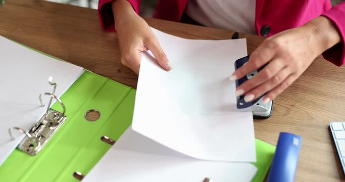 Female hands of accountant or secretary are punching holes with hole punch in documents in office