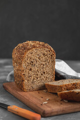 Sliced rye bread with seeds on a wooden board on a grey background. Copy space.