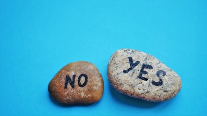 Two grey pebbles with the text yes and no on a blue table.