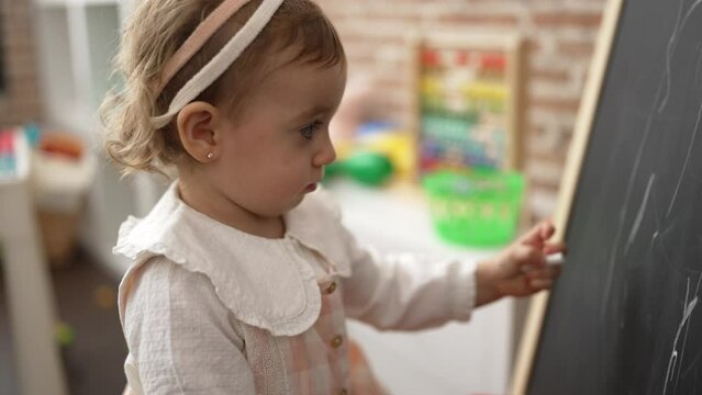 Adorable caucasian girl drawing on blackboard standing at kindergarten