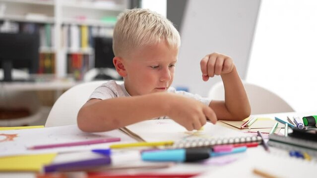 Adorable toddler student drawing on notebook sitting on table at classroom