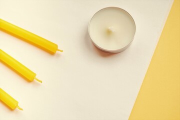 Round white and three yellow candles on white yellow table