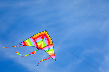 rainbow colored kite flying high in the blue sky with some white clouds