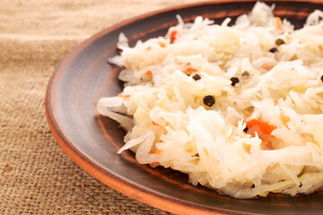 Sauerkraut in a clay plate on a jute cloth, macro.