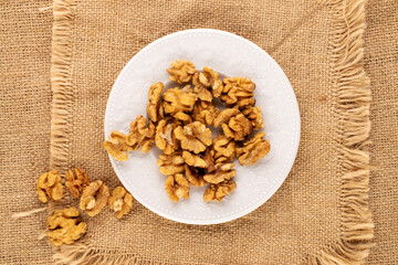 A few peeled walnuts in a white ceramic plate on a jute cloth, macro, top view.