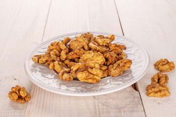 Several peeled walnuts in a white ceramic plate on a wooden table, macro.