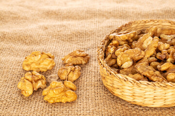 A few peeled walnuts in a straw plate on a jute cloth, macro.