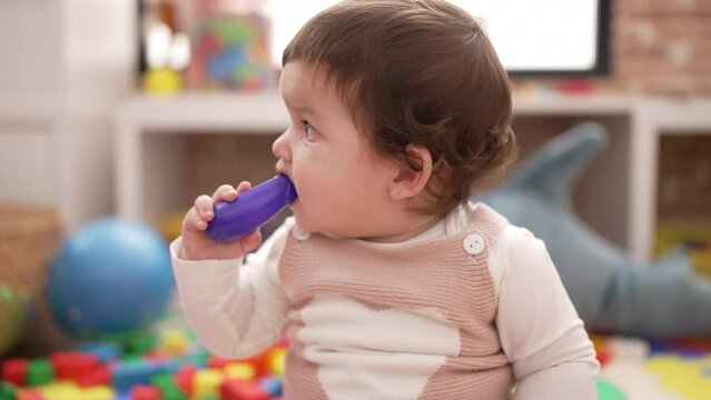 Adorable toddler bitting plastic food toy sitting on floor at kindergarten