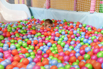 Fototapeta na wymiar A boy in a dry paddling pool in playing centre with plastic balls.