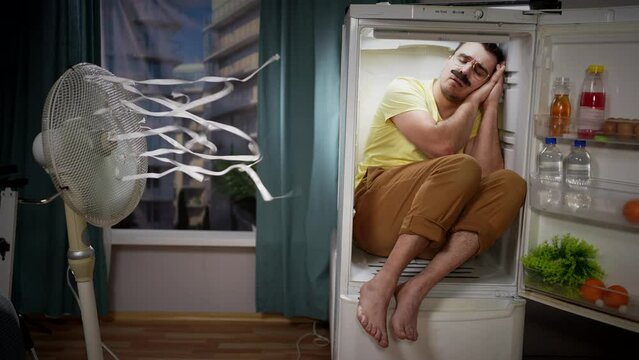 problem of hot weather, a male freak with a mustache suffering from heat and overheating in a hot summer, sleeps in the refrigerator