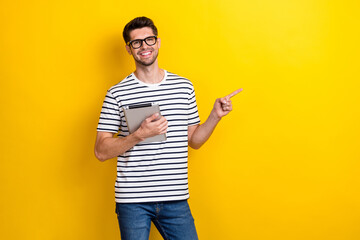 Portrait of handsome positive guy hold tablet direct finger empty space isolated on yellow color background