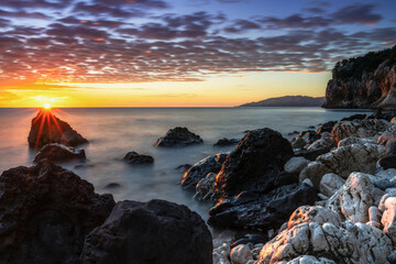 colorful sunrise at Cala Gonone with black and white rocks and boulders in the foreground