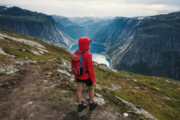 Young tourist woman in red jacket watching the view on the beautiful Ringedalsvatnet Lake. Hiking in Norwegian nature in windy weather. 