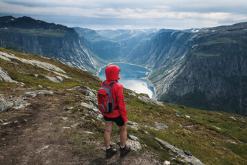 Young tourist woman in red jacket watching the view on the beautiful Ringedalsvatnet Lake. Hiking in Norwegian nature in windy weather. 