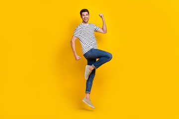 Fototapeta na wymiar Full length photo of cool lucky guy dressed striped t-shirt rising fist jumping high isolated yellow color background