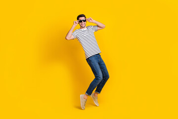 Full length photo of pretty funny guy dressed striped t-shirt dark eyewear having fun dancing isolated yellow color background