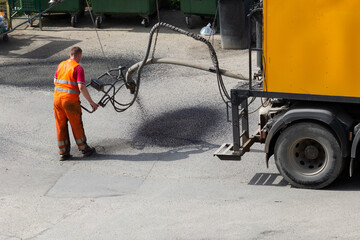 An employee of the road service fills the hole in the road surface with emulsion with rubble with a...