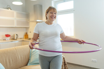 Overweight mature woman in white t-shirt and gray leggings trying to lose weight with hula hoop exercises © SOLOTU