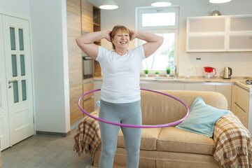 Overweight mature woman in white t-shirt and gray leggings trying to lose weight with hula hoop exercises © SOLOTU
