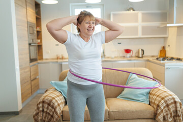 Overweight mature woman in white t-shirt and gray leggings trying to lose weight with hula hoop exercises © SOLOTU