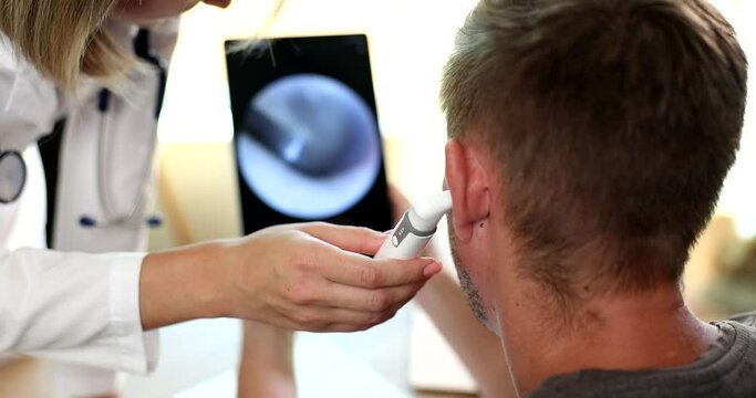 Otorhinolaryngologist examines patient ear using digital otoscope with image