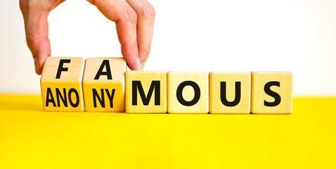 Famous or anonymous symbol. Concept word Famous and Anonymous on wooden cubes. Businessman hand. Beautiful yellow table white background. Business famous or anonymous concept. Copy space.