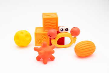 Three sensory balls in different warm colors, three silicone soft cubes and a crab-shaped rattle. Tactile toys for the development of babies from three months - obrazy, fototapety, plakaty