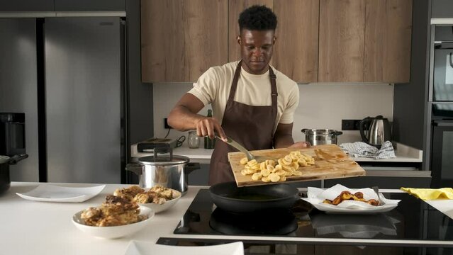 Young black man frying plantains slices in a kitchen.
