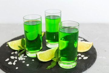 Sweet refreshing mint liqueur, with ice and mint leaves on table background, Shots with lime slice and mint flat lay
