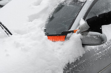 Cleaning snow from the windshield of a car with a brush during a snowfall.Snow cyclone.